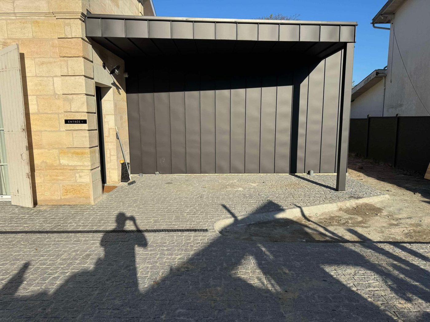 Abri de cour à toiture métallique à joint debout anthracite sur une cour pavée, réalisé par A2Roulet-Toiture